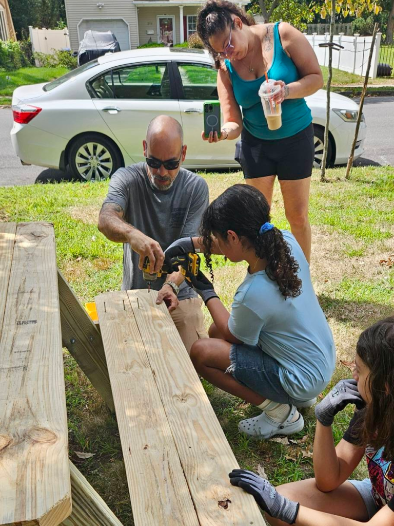 Girl Scouts and adult volunteers use power tools to assemble a picnic table at Girl Scout Park in Rahway