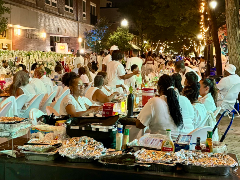 Guests enjoy food at Rahway’s Soiree en Blanc, with dishes laid out along a community table.