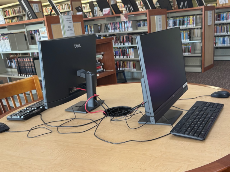 Two new Dell desktop computers on a wooden table inside the Rahway Public Library.