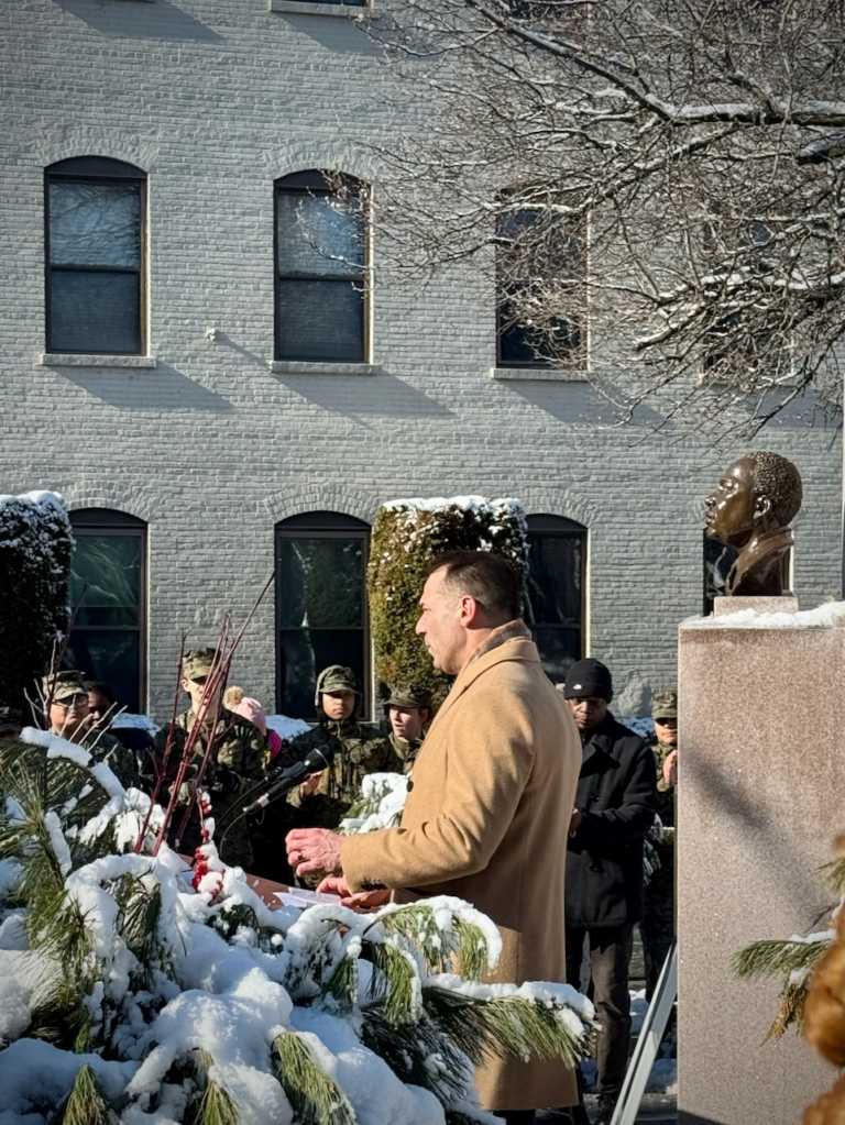 A local official speaks during a Martin Luther King Jr. Day ceremony at MLK Park in Rahway, with the Dr. King statue and attendees gathered on a winter morning.